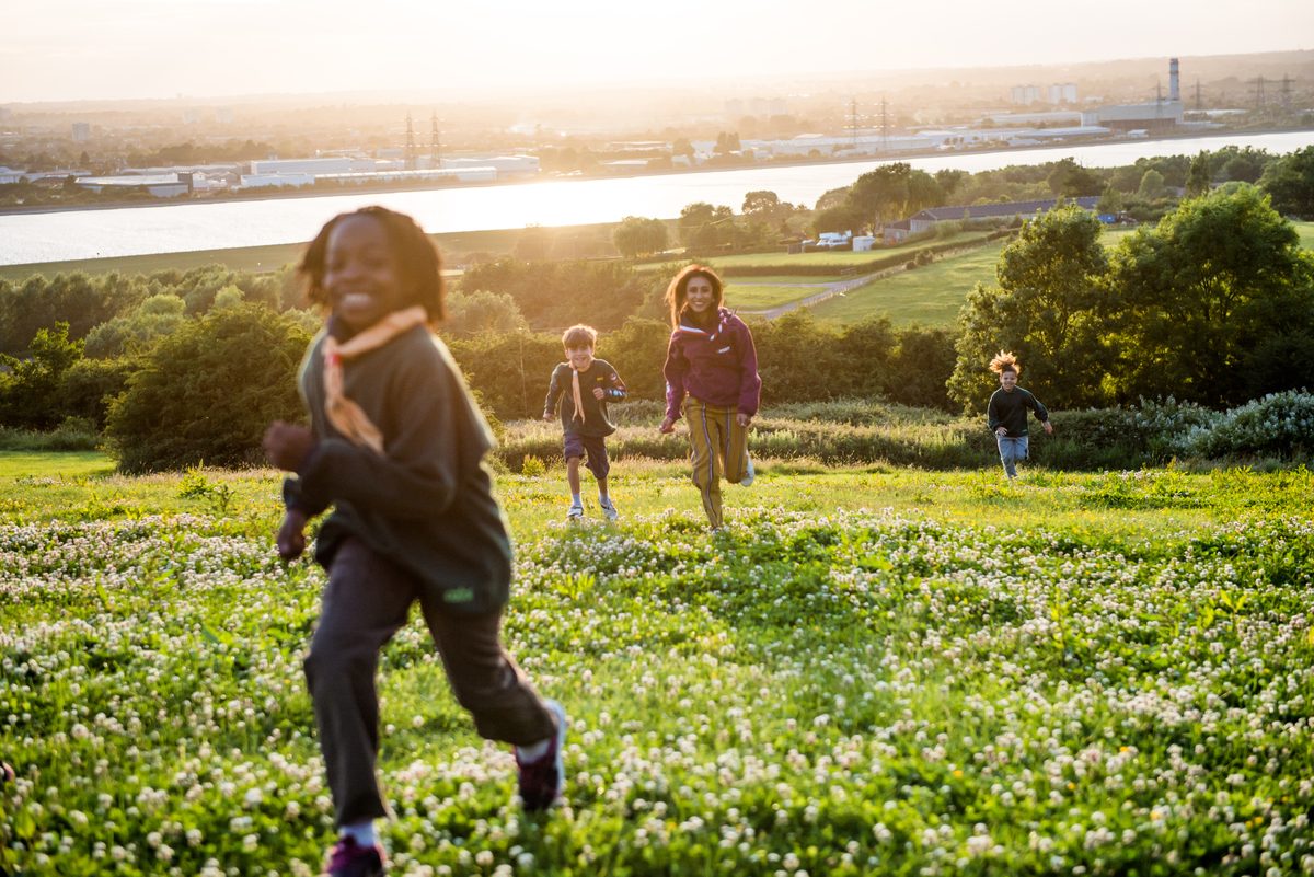 A mixed-age group of young people and a volunteer running together across a meadow at sunset