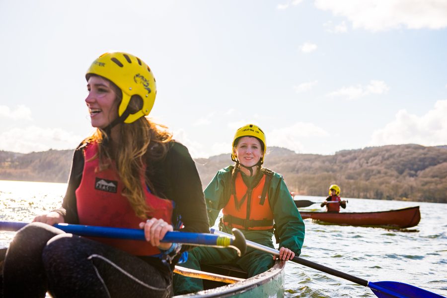 Two canoeists in helmets and life jackets paddling on a lake