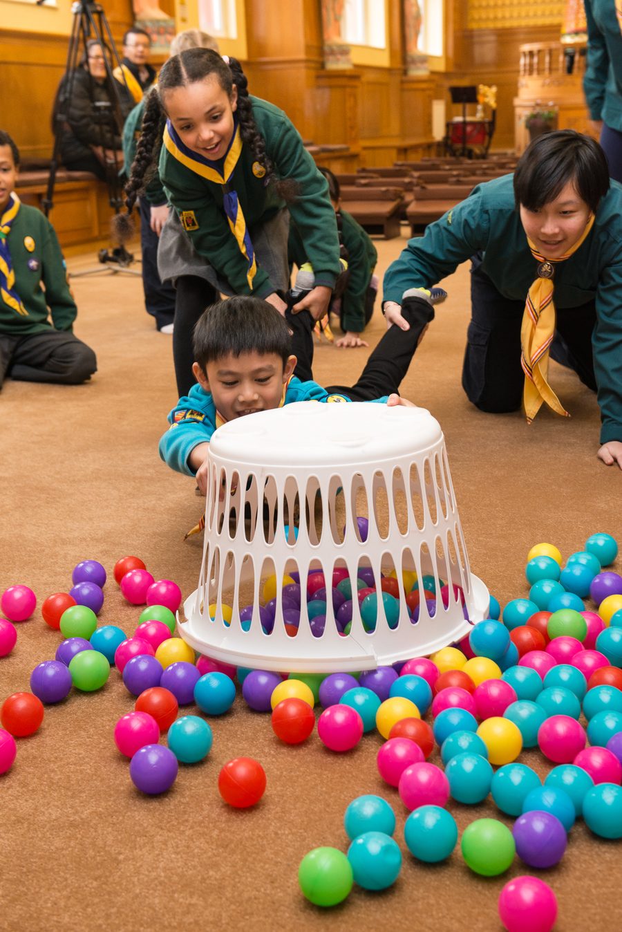 A Beaver Scout in a turquoise uniform diving into a ball pit game indoors