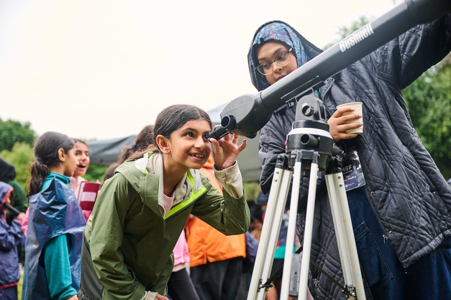 A young Beaver looking through a telescope with a volunteer's help outdoors
