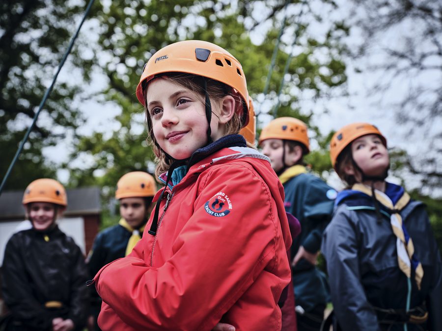 A group of Cub Scouts in orange helmets on an outdoor high ropes challenge
