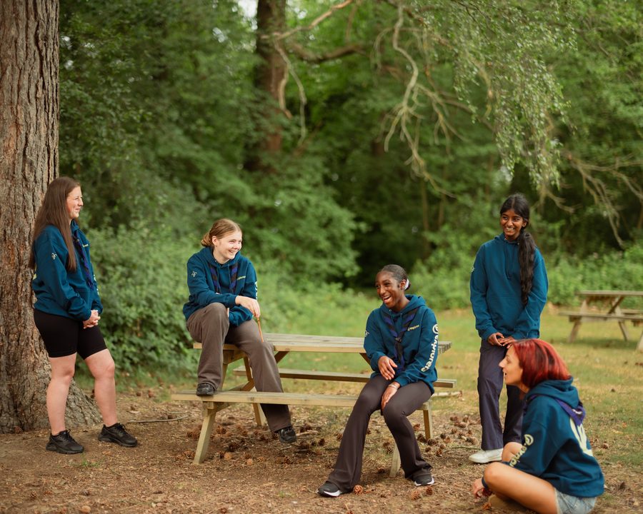 A group of Explorer Scouts chatting together around a picnic table outdoors