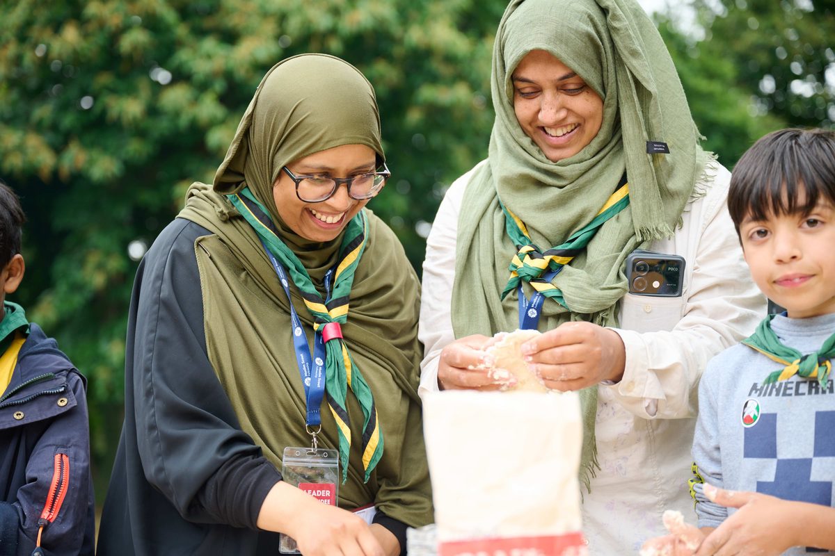 Two volunteer leaders and a young person kneading dough together outdoors