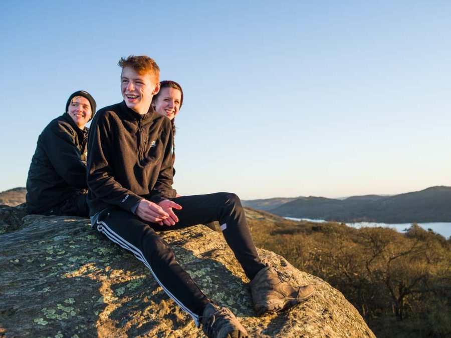 Young people sitting together on a rock at dusk, overlooking hills and a lake