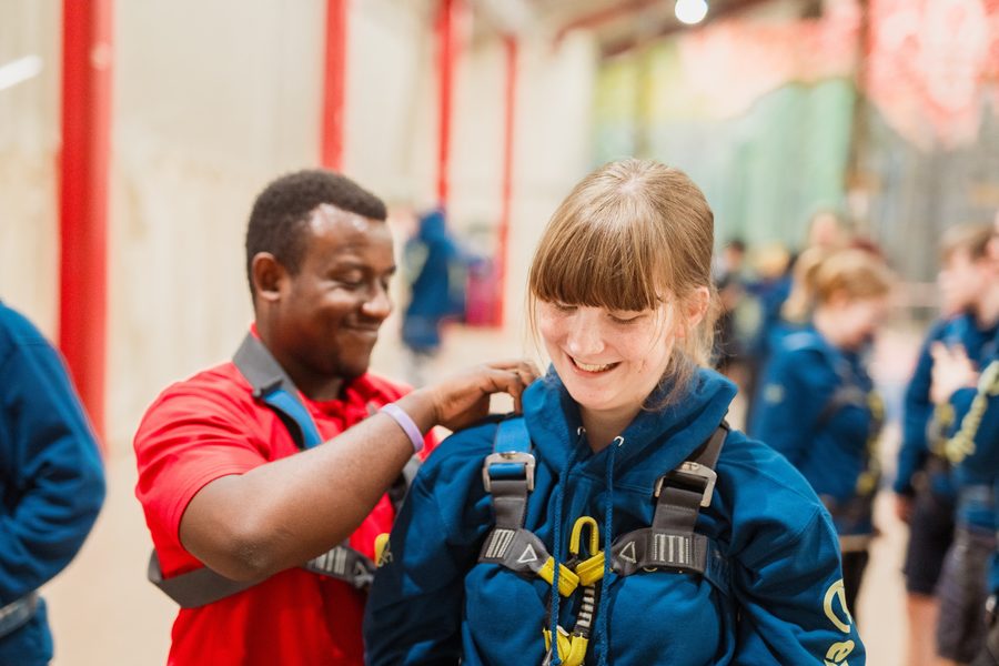 A young leader being helped into a climbing harness by a volunteer instructor