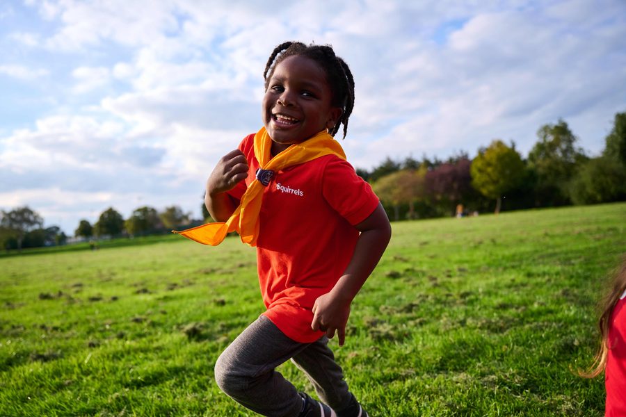 A young Squirrel in red uniform running and smiling across a field
