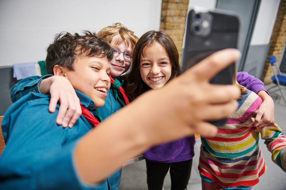 Three young people laughing together while taking a group selfie