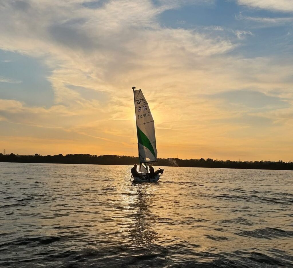 A First Luton Sea Scouts sailing dinghy on the water at sunset