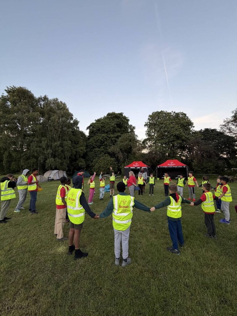 St Joseph's Scouts holding hands in a circle at camp as the sun sets